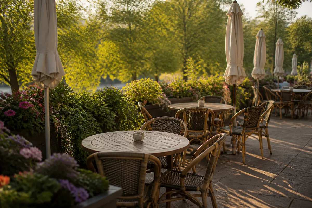 Terrasse de restaurant avec tables en bois, parasols repliés et jardinières fleuries